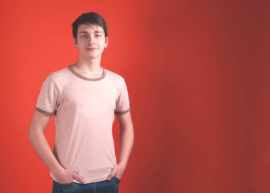 bej t shirt emin genç adam ceplerinde elleri ile ayakta ve kopya alanı ile mercan rengi arka plan üzerinde kamera bakıyor