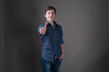 mavi kendine güvenen yakışıklı genç adam kamera bakıyor ve kopya alanı ile gri arka plan üzerinde başparmak