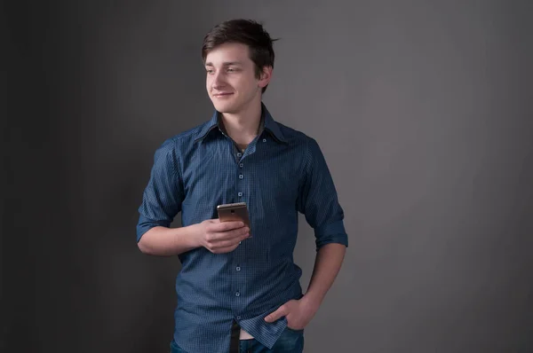 Jovem Bonito Camisa Azul Segurando Smartphone Olhando Para Fundo Cinza — Fotografia de Stock