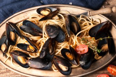 metal plaka ve ahşap dokusal arka plan üzerinde deniz ürünleri ve dilimlenmiş kiraz domates ile lezzetli makarna üst görünümü