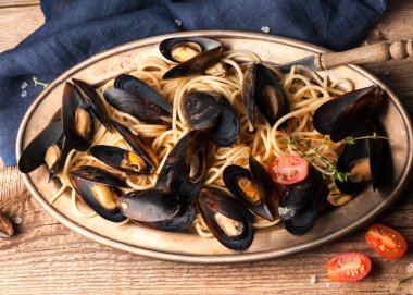 ahşap arka plan üzerinde mavi bez yakın metal plaka üzerinde sos pişmiş lezzetli geleneksel İtalyan spagetti ve midye üst görünümü