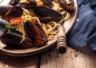 ahşap arka plan üzerinde çatal ile metal altın plaka siyah kabukları midye ile lezzetli İtalyan makarna