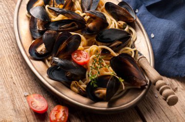 siyah kabukları midye ile lezzetli İtalyan makarna yüksek açı görünümü ve ahşap arka plan üzerinde metal altın plaka kesilmiş domates