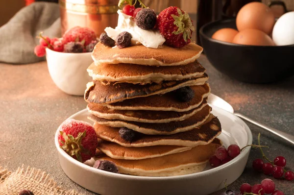 side view of delicious american pancakes on white plate decorated with sour cream and fresh berries on table