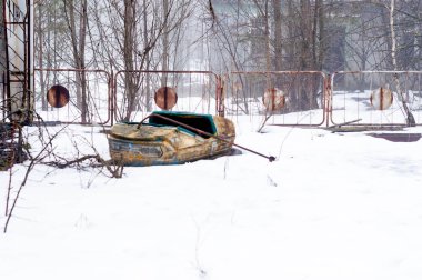 Pripyt, yabancılaşma Çernobil bölgesinde ağaçlar ve çit froont terk edilmiş eğlence parkı kar üzerinde paslı sarı cazibe araba