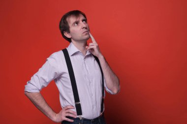 pembe gömlek ve siyah askılı yanak üzerinde el ve parmak ile yakışıklı kendine güvenen adam uzağa bakıyor ve kopya alanı ile turuncu arka plan üzerinde düşünme