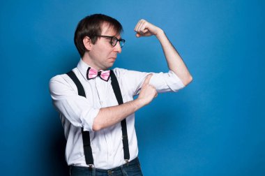 kolları, papyon, siyah askı ve gözlük grimacing ve mavi arka plan üzerinde pazı ölçme ile pembe gömlek zor adam