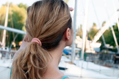 At kuyruklu bir kadının arkadan görünüşü. Teknelerin ve nehirdeki gökyüzünün önünden uzağa bakıyor.