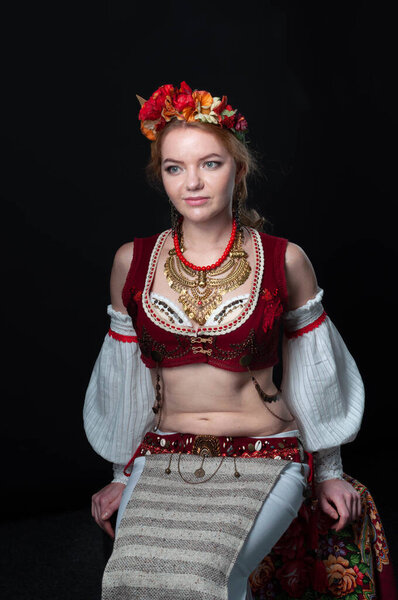 beautiful woman in traditional ukranian dance costume with golden necklace, circlet of flowers, red west, white sleeves and skirt 