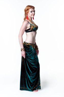 Yeşil göbek dansı kostümlü ve kırmızı küpeli güzel bir kadın beyaz arka planda dikiliyor ve diğer tarafa bakıyor.