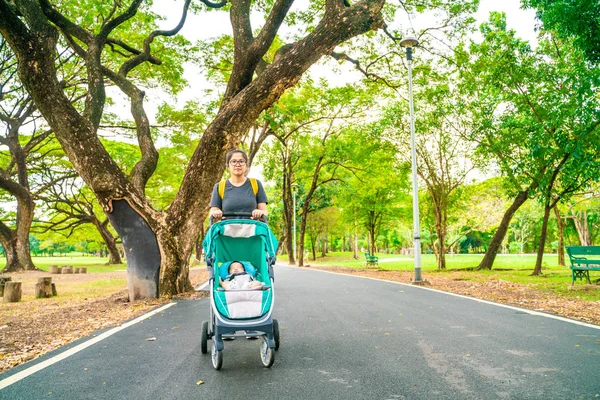 Mother with baby infant recreation in green park with stroller relax