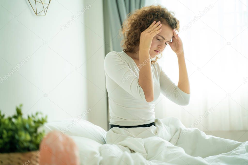 Women sitting on bed holding her head have a headache with migraine