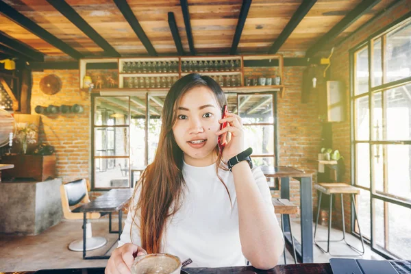 美しいアジア ビジネスの女性は ラテのコーヒーを飲みながらカフェで座っているスマート フォンを使用します — ストック写真