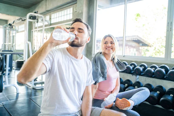 Athletic young couple relax and drinking water after work out in gym, Caucasian sport people