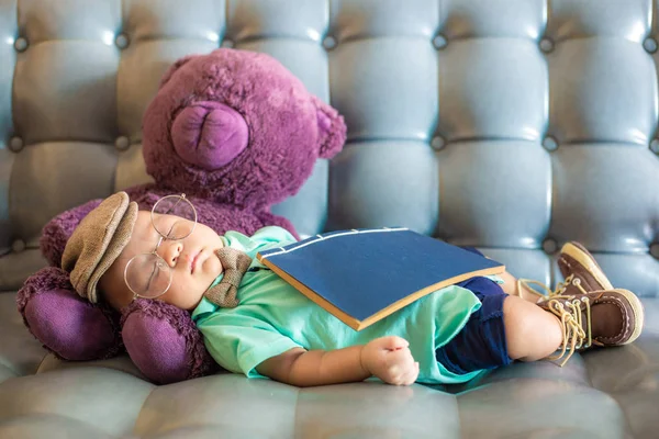 Adorable baby boy sleeping on vintage sofa with book and doll, Student costume
