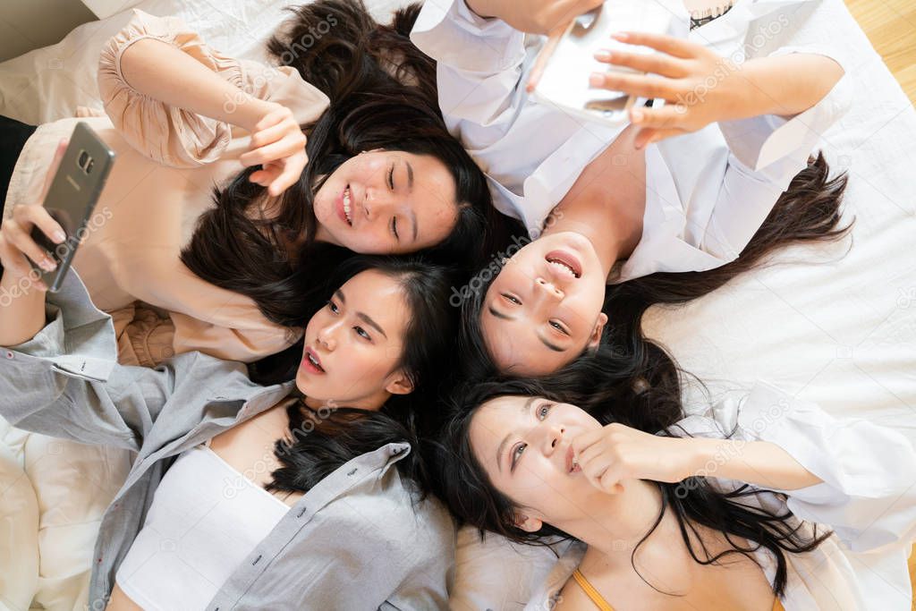 Top view group of asian beautiful smiling women lying on bed use