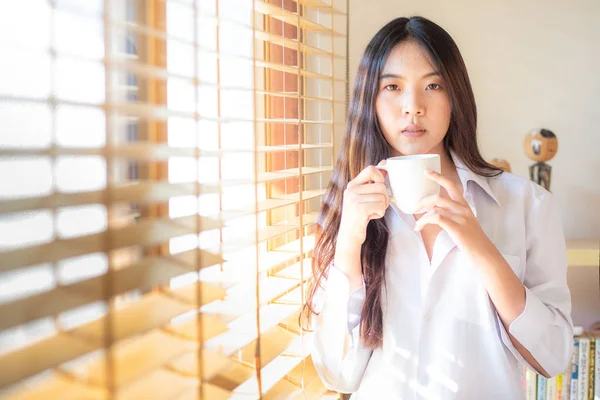Hermosas mujeres asiáticas jóvenes sostienen taza de café de pie cerca de ganar —  Fotos de Stock