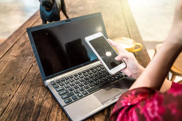 Női kéz használata okostelefon és a laptop számítógép kávéscsésze — Stock Fotó