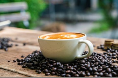 Ahşap masada kahve çekirdeği ile Latte sanat kahve fincanı