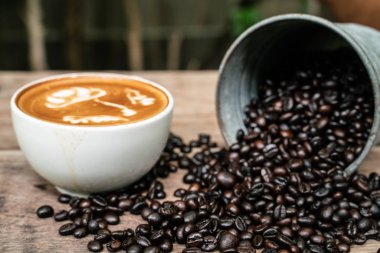 Ahşap masada kahve çekirdeği ile Latte sanat kahve fincanı