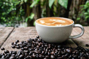 Ahşap masada kahve çekirdeği ile Latte sanat kahve fincanı