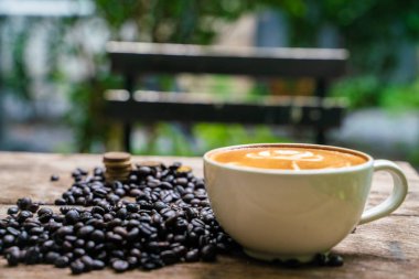 Ahşap masada kahve çekirdeği ile Latte sanat kahve fincanı