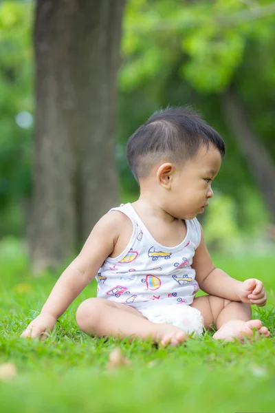 Adorabile bambino seduto nel campo del parco verde — Foto Stock