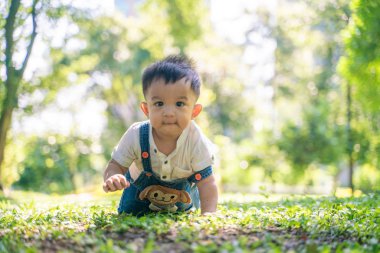 Şehir parkında yeşil çimlerde sürünen komik çocuk.