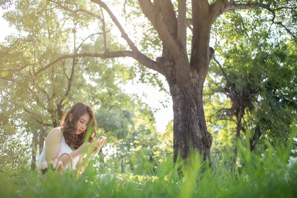 Mooie Aziatische Vrouwen Zitten Onder Boom Groen Gras Gebruik Smartphone — Stockfoto