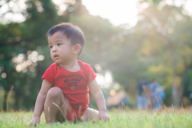 Yeşil çayırlarda sürünen komik Asyalı çocuk. Gün batımı bebek egzersizi.