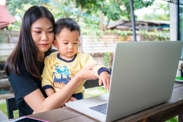 Smart young asian mom hold baby boy use laptop computer in cafe outdoor activity