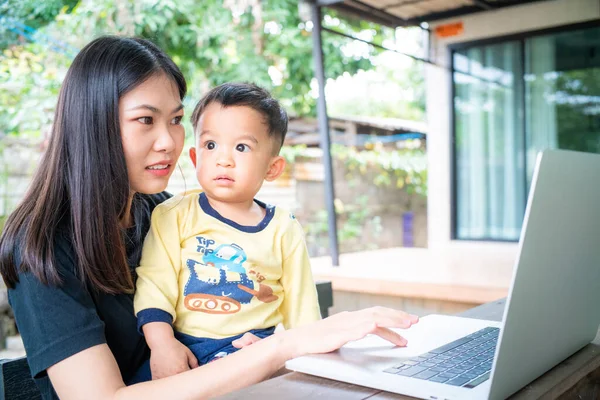 Smart young asian mom hold baby boy use laptop computer in cafe outdoor activity