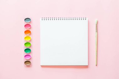 Suluboya paletleri, boya fırçası, beyaz kağıt Yaratıcı düz yatıyordu. Pembe pastel arka plan üzerinde Sanatçı işyeri.