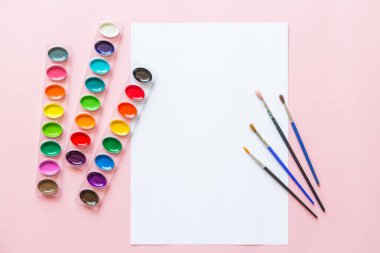 Suluboya paletleri, boya fırçaları, beyaz kağıt Yaratıcı düz yatıyordu. Pembe pastel arka plan üzerinde Sanatçı işyeri.