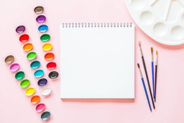 Suluboya paletleri, boya fırçaları, beyaz kağıt Yaratıcı düz yatıyordu. Pembe pastel arka plan üzerinde Sanatçı işyeri.