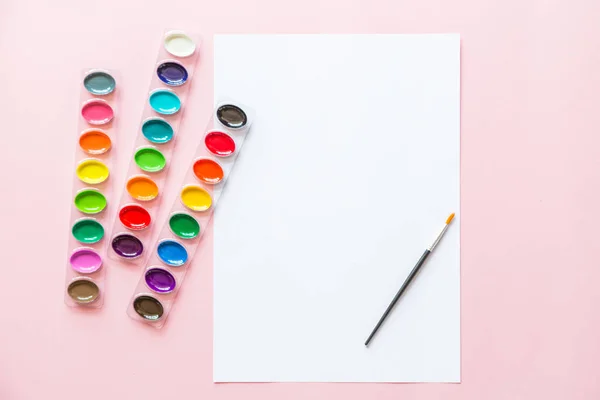 Kreativní ploché barvy barevných palet, nátěrových barev, bílé noviny. Umělecké pracoviště na růžovém pastelu. — Stock fotografie