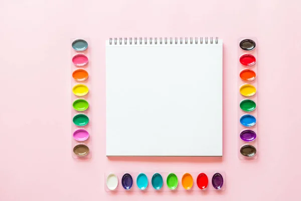 Kreatywne płaskie lay akwarela palety i notebooka. Miejsce pracy artysty na różowym tle pastelowych. — Zdjęcie stockowe