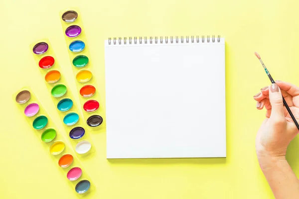 Tvořivé ploché barvy barevných palet, notebooků, ručního držení kartáče. Pracoviště interpreta na žlutém pozadí. — Stock fotografie