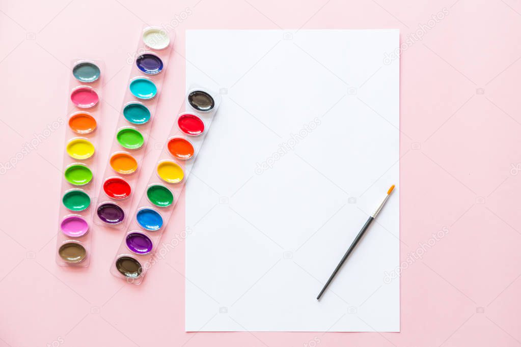Creative flat lay of watercolor palettes, paint brushe, white paper. Artist workplace on a pink pastel background.