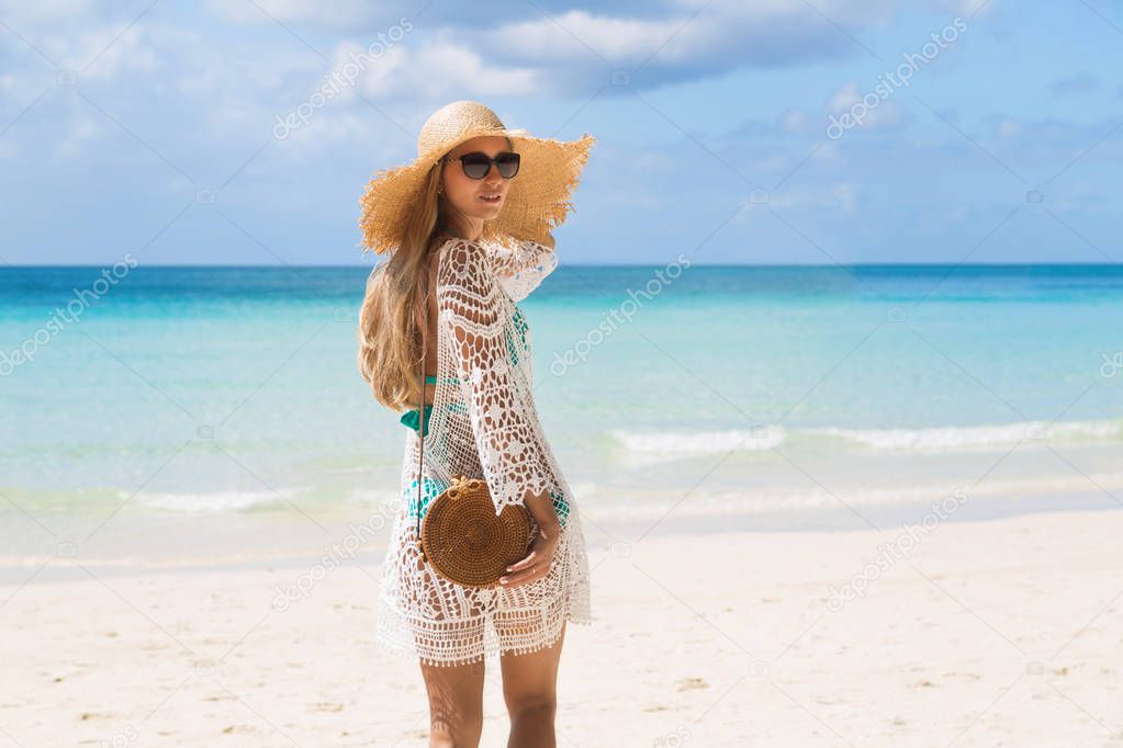 Sexy tanned girl in blue bikini and white tunica standing on the seashore. Beautiful model sunbathes and rests on sea. Concept vacation, travel