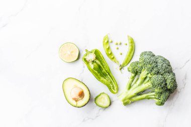 Taze avokado, limon, brokoli, bezelye, salatalık, yeşil biber. Düz yatıyordu. Gıda konsepti. Beyaz mermer arka plan üzerinde yatan yeşil sebzeler