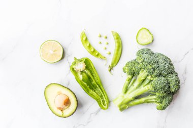 Taze avokado, limon, brokoli, bezelye, salatalık, yeşil biber. Düz yatıyordu. Gıda konsepti. Beyaz mermer arka plan üzerinde yatan yeşil sebzeler