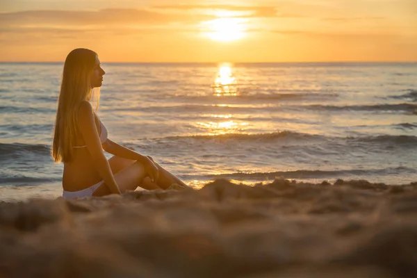 Moda foto ao ar livre de menina bonita sexy com cabelo loiro em elegante biquíni branco relaxante na praia do pôr do sol — Fotografia de Stock