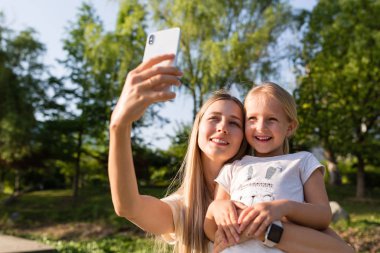 Güzel genç anne ve kızı açık cep telefonu kullanarak sarı saçlı. Parkta selfie çeken şık kızlar. Teknolojiyi kullanan kişiler 