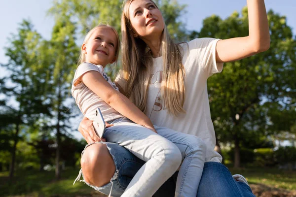 Mooie jonge moeder en dochter met blond haar omarmen outdoor. Stijlvolle meisjes maken wandelen in het Park. Familieconcept — Stockfoto