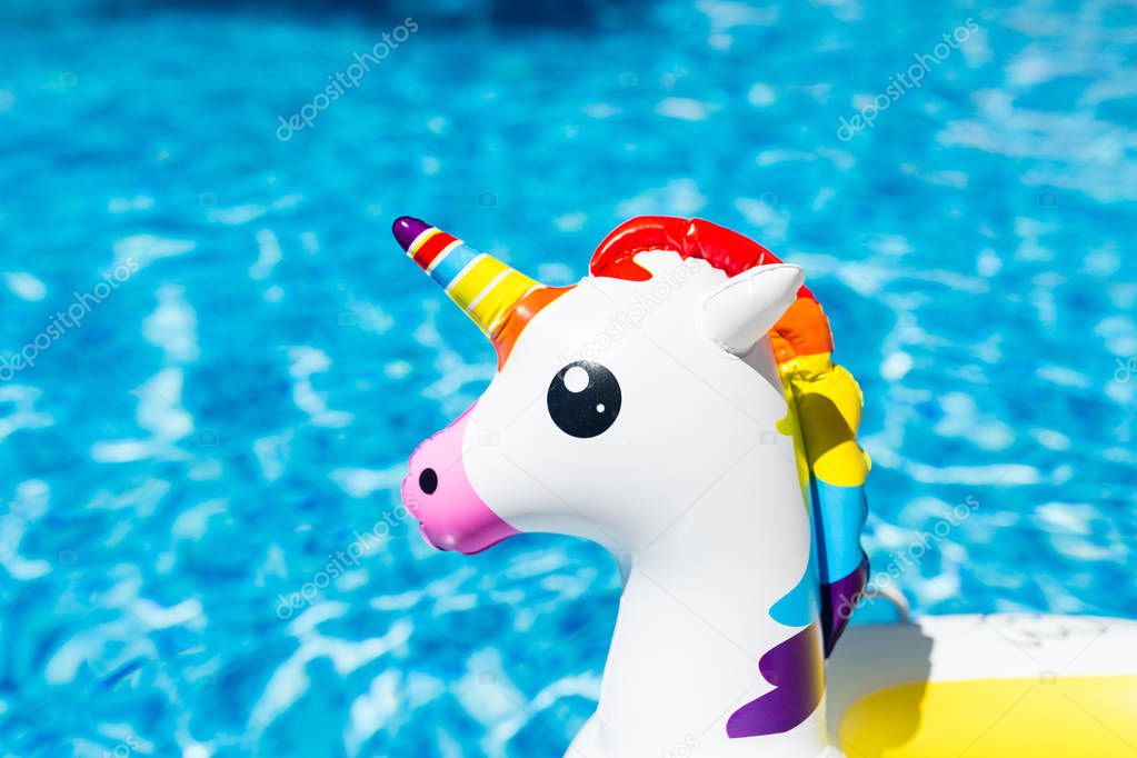 Inflatable colorful white unicorn at the swimming pool. Summer time in the swimming pool with plastic toys. Summer vacation, Relaxation and fun concept