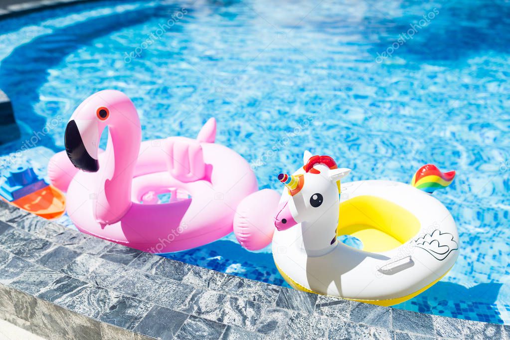 Inflatable colorful white unicorn and pink flamingo at the swim pool. Summer time in the swimming pool with plastic toys. Relaxation and fun concept