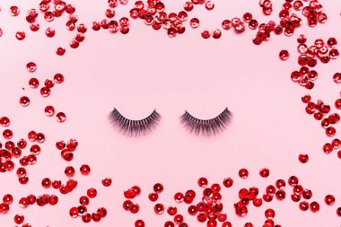 Yanlış kirpik siyah renk ve kırmızı konfeti pembe arka planda yatıyor. Güzellik ve makyaj konsepti. Flatlay, mockup, tepegöz, üst görünüm kopya alanı