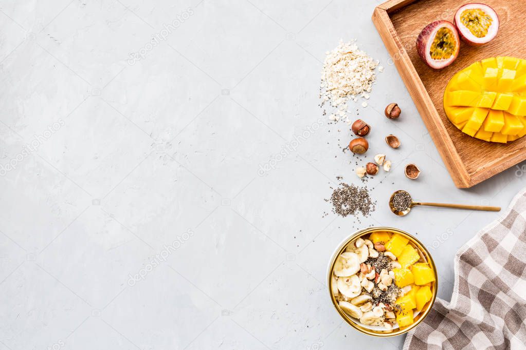 Breakfast oatmeal porridge with fresh fruits, chia seeds and hazelnut on gray background. Oatmeal with mango and banana. Healthy breakfast concept. Top view, flat lay, mockup, overhead, copy space