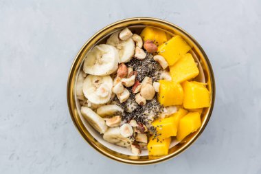 Taze meyveler, Chia tohumları ve gri arka planda fındık ile kahvaltı yulaf püresi. Mango ve muz ile yulaf ezmesi. Sağlıklı kahvaltı konsepti. Üst görünüm, düz yatıyordu, mockup, yük, kopya alanı